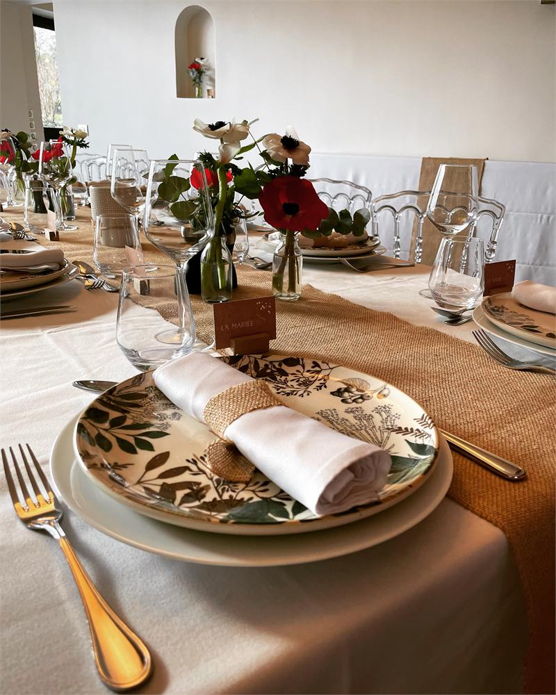 Art de la table pour un mariage champêtre : assiette fleurie, serviette nouée et bouquet de saison