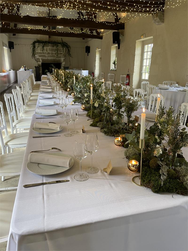 Grande tablée de mariage sous guirlandes lumineuses, centre de table végétal et bougies