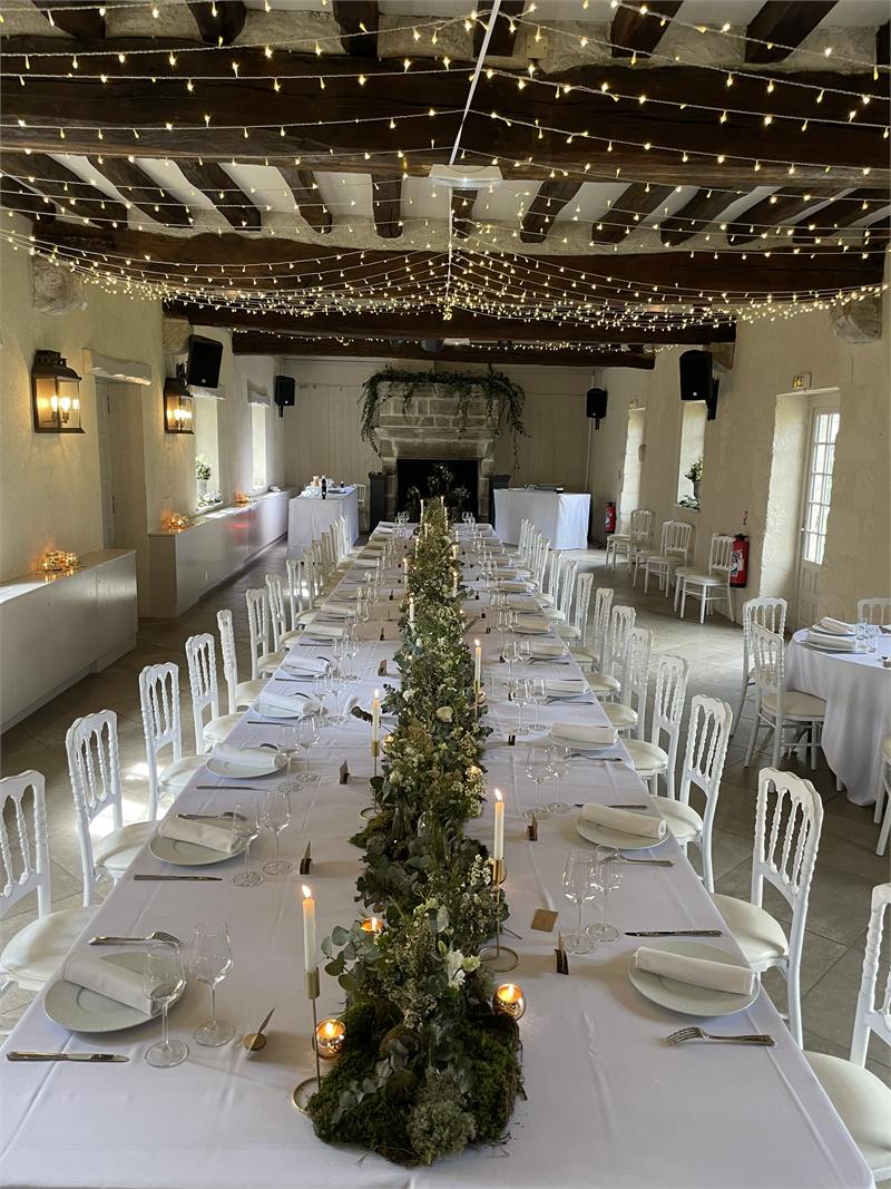 Salle de réception de mariage avec tables en longueur et guirlandes lumineuses